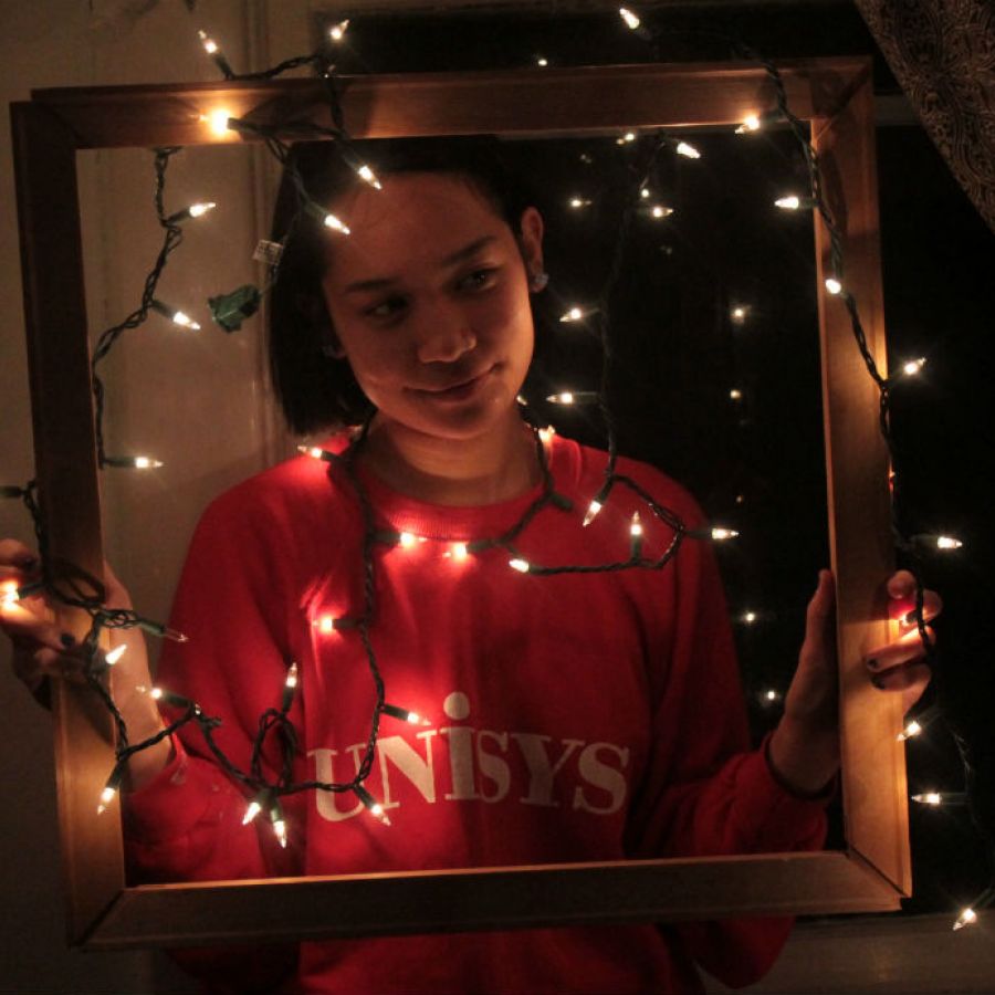 A photo of a woman holding a picture frame around her with string lights on the frame