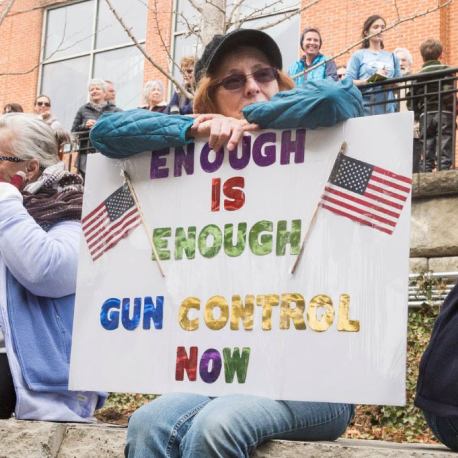 A photo of a person holding a sign that reads "Enough is Enough, Gun Control Now"
