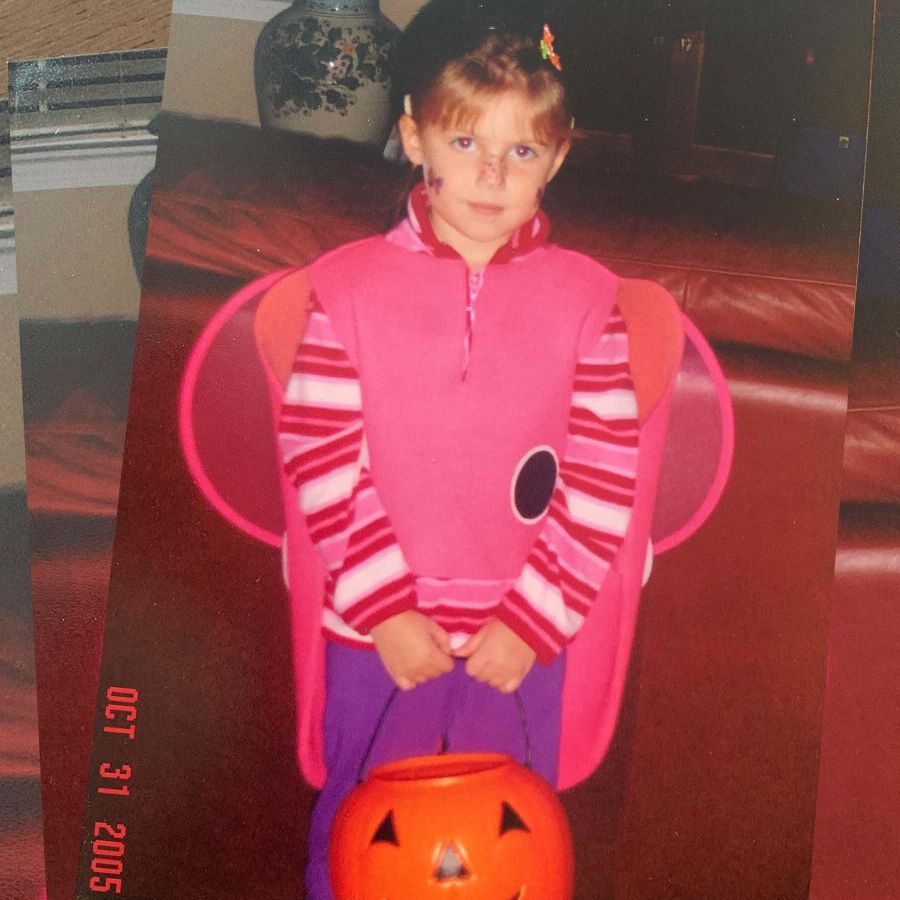a girl in a costume with wings holds a pumpkin shaped trick or treat bag