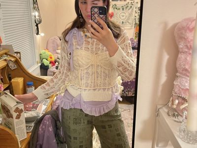 Ella wearing green pants and a cream corset overlaid a crochet cream top and a purple ruffle tank top